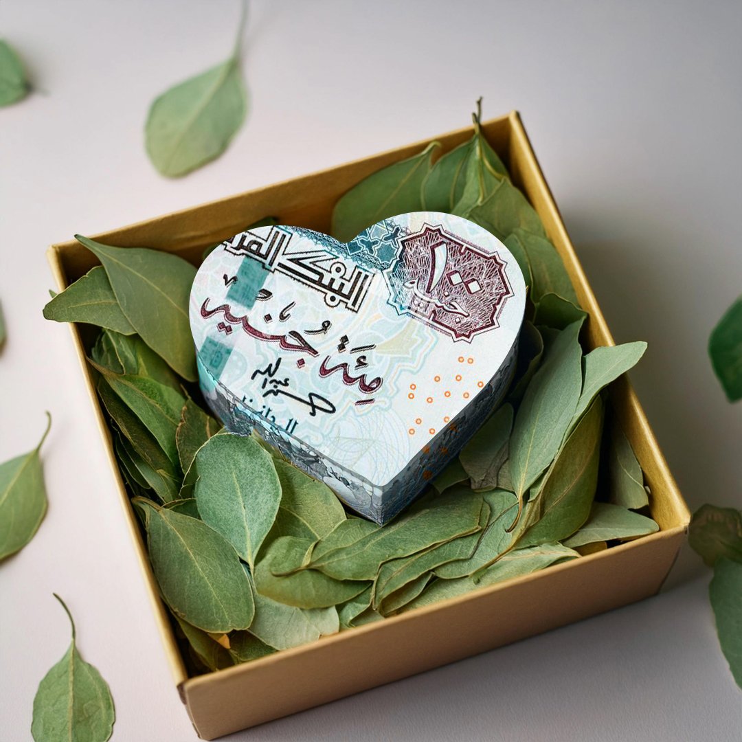 a lot of Egyptian Pounds folded into heart shape into a box filled with green leaves